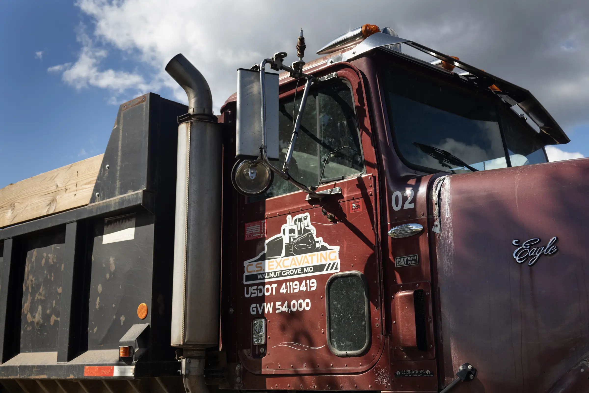 red dump truck with a black steel bed parked outdoors under a partly cloudy sky