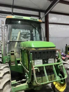 green farm tractor with large front tires parked on concrete floor inside a metal equipment building