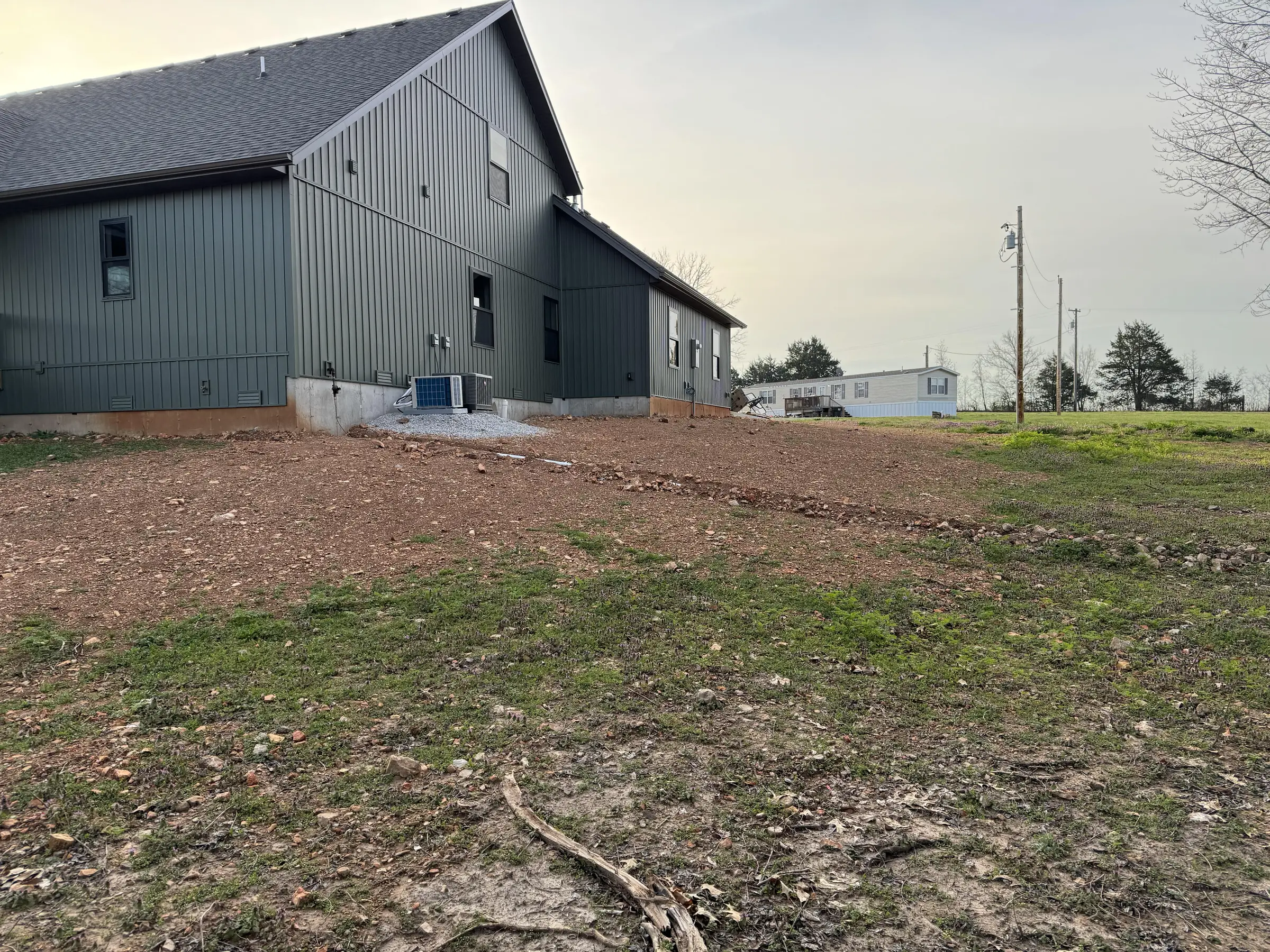 freshly graded dirt slope beside a gray metal building with sparse grass and utility poles in the background